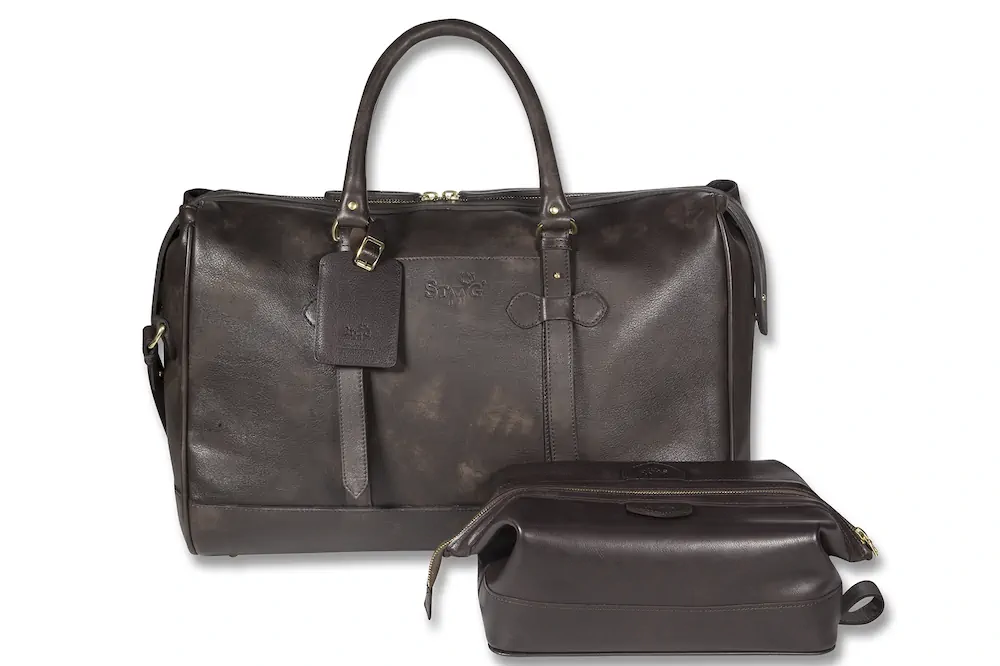 Dark brown leather duffle bag and matching toiletry bag on a white background.