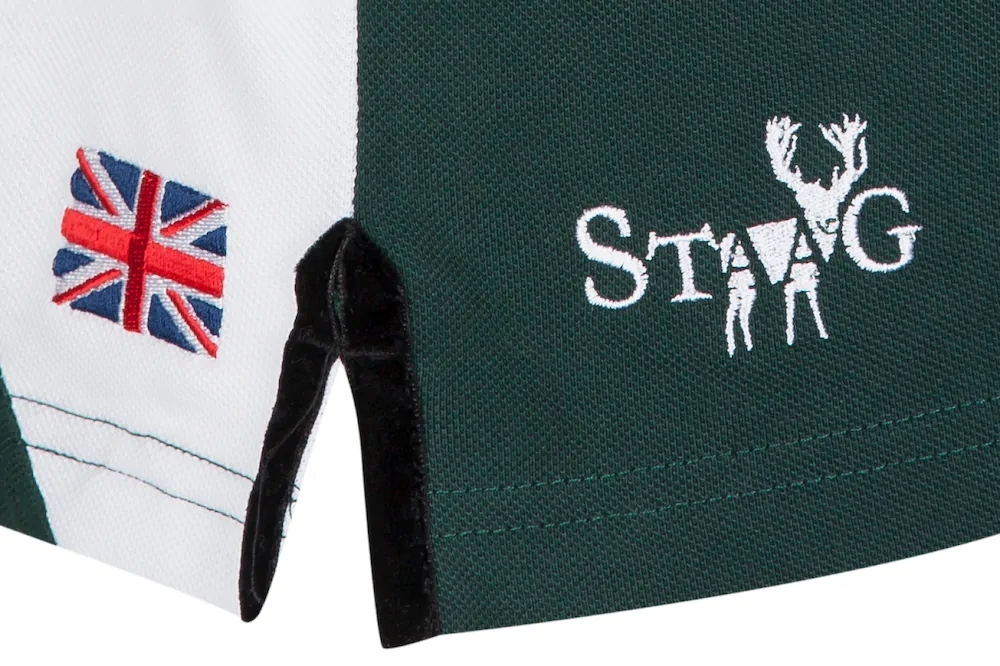 Close-up of a garment's hem showing a United Kingdom flag patch and the word 'STAG' embroidered with a silhouette of hunters and a stag integrated into the letters.